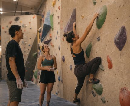 Three friends at an indoor bouldering gym cheering on a climber.